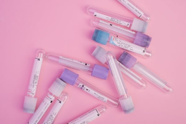 A collection of empty blood vials against a pastel pink background